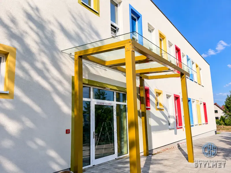 Żółte zadaszenie stalowe nad wejściem do budynku